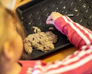 Ein Kind formt Sand auf einer schwarzen Unterlage.