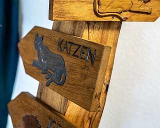 Detailaufnahme eines Holzschildes mit dem Wort &#039;Katzen&#039; und einer Katzenzeichnung.