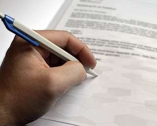 Eine Hand hält einen Stift und schreibt auf einem Blatt Papier.